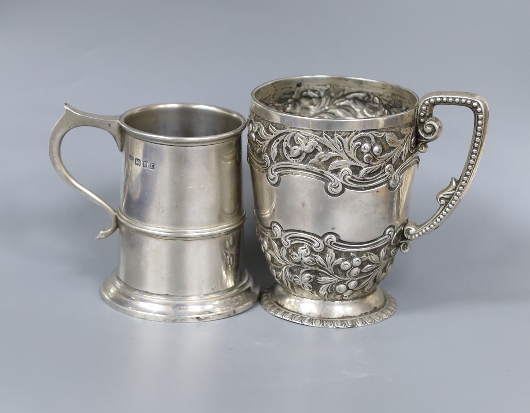 A late Victorian embossed silver christening mug, London, 1895, 10.5cm and a similar later silver mug, 10.5oz.